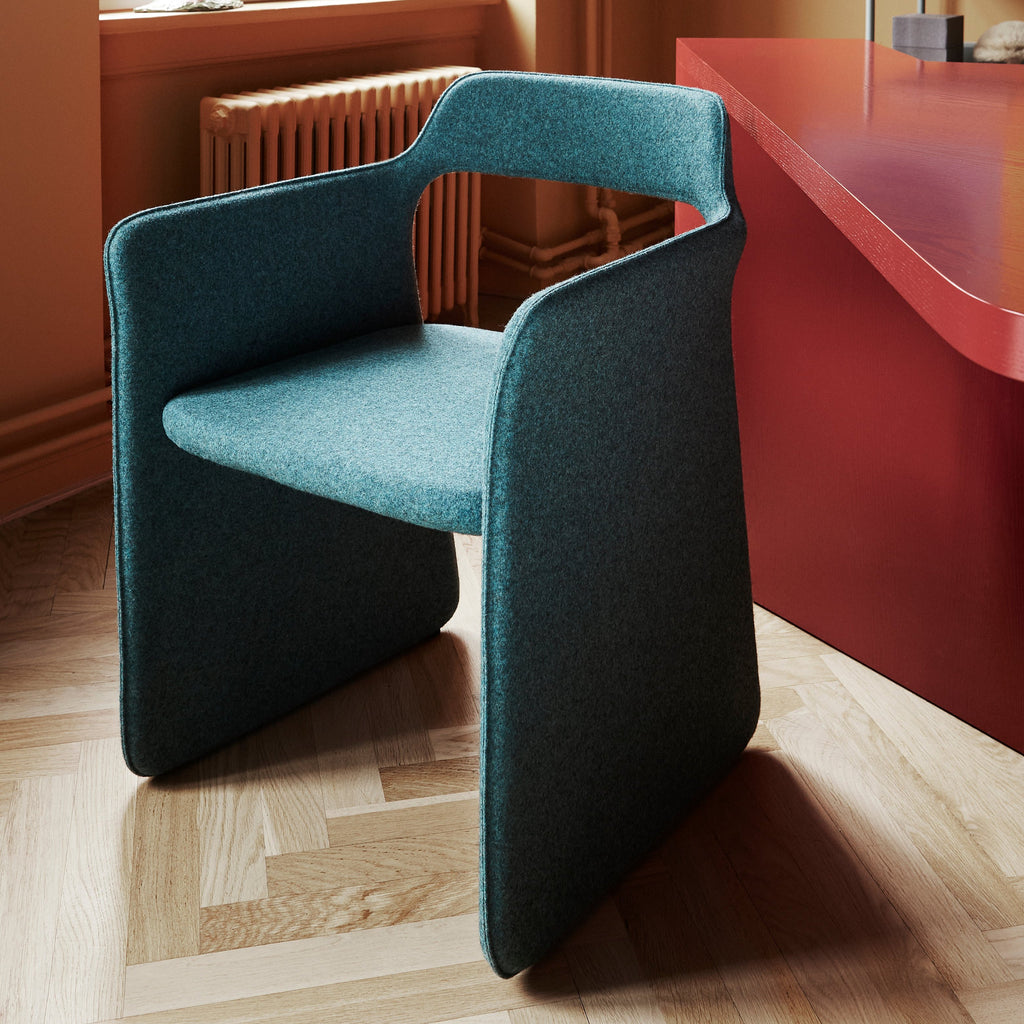 An elegant dining chair in dark turquoise colour next to a dining table in deep red colour. Hardwood floors.