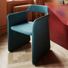 An elegant dining chair in dark turquoise colour next to a dining table in deep red colour. Hardwood floors.