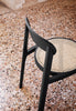 A close up view from above of an elegant dining chair. Dining chair is made from black wood with a light coloured seat. Terrazzo floor.