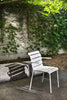 A beautiful white garden chair with arms in a wonderful garden on a summer day. Sun casts shadows from the chair. Lot of leafs in the background.