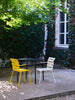 Beautiful outdoor furniture in a gorgeous garden on a sunny summer day. Yellow chair, black table and white chair. Leafy trees.