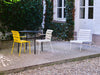 Beautiful outdoor furniture in a gorgeous garden on a sunny summer day. Yellow chair, black table, white chair and a white lounge chair. Leafy trees.