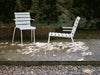 A white outdoor chair and a white outdoor lounge chair in a beautiful European garden on a sunny summer day.