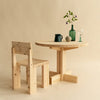 Studio image. 001 Dining chair and dining table. Both made from sustainably grown pine. Beige background. Some small home items on top of table.