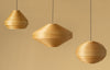 Three skandinavisn pendant lights hanging in a row. The lights are made from bend pine veneer. Light beige background.