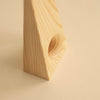 Close up of a pine doorstop. The doorstopper stands tall on its wider end. The wider end has a hole in it. Beige background.