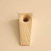 Pine doorstop. One end is wide with hole in it. It then tapers gradually towards the other end. Beige background.