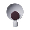 Product photo. A cute circular table lamp on a white background. The table lamp is in light grey colour. The light source is in the middle of the lamp and also circular. Light source is in dark burgundy colour.