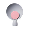 Product photo. A cute circular table lamp on a white background. The table lamp is in light grey colour. The light source is in the middle of the lamp and also circular. Light source is in light pink colour.
