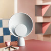 Cute light grey circular table lamp on a table. Colourful shapes in the background.