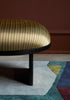 Arqui 2 gólfteppi frá Please Wait To Be Seated. Abstrakt form. Bekkur með mynstruðu áklæði. Nærmynd. Dökkrauður veggur í bakgrunni.