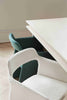 Two dining chairs of the same kind, side by side next to a white dining table. The chair in the foreground is white and the chair in the background is green.