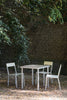 A beautiful garden on a sunny summer day. Minimalistic but colourful outdoor furniture in aluminium. Ivory coloured table top. Three modern chairs around the table. Brick wall and leafy trees in the background.
