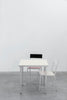 Modern and minimalistic aluminium furniture. A small dining table with square table top in the colour ivory. Two dining chairs. Grey concrete floor. A white wall in the background.