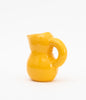 A yellow, glossy and cartoonish ceramic jug. White background.