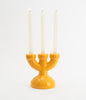 The cutest little, three spoke candlebra in yellow ceramics. White candles. White background. The candles are lit.