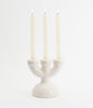 A pretty little, three spoke candlebra in white ceramic with white candles. The candles are lit. Background is white.