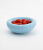 A round, baby blue ceramic bowl on a white background. The bowl is filled with small cherry tomatoes.