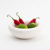 A white ceramic bowl with soft shapes. Red peppers and limes are in the bowl. White background.