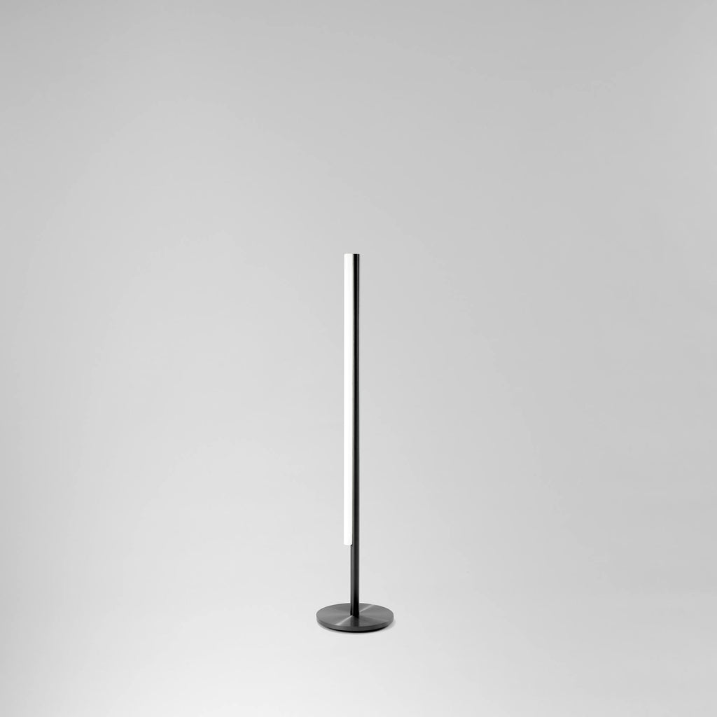 Grannur og fágaður gólflampi úr svörtu satin áli frá Michael Anastassiades. Ljós grár bakgrunnur.
