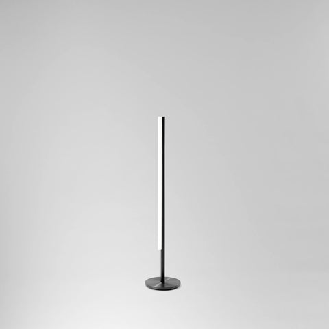 Grannur og fágaður gólflampi úr svörtu satin áli frá Michael Anastassiades. Ljós grár bakgrunnur.