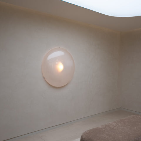 Large circular wall light with mild light. Bright room. White wall. Some light from above.