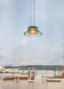 Glass pendant light fixture hanging above a table with a scenic view of water and buildings in the background.