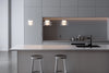 Three glass pendant lights hanging in a modern kitchen with gray cabinets, a island, and bar stools.