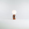 A beautiful table lamp. Soft and gentle shapes. The body of the lamp is in copper and the shade is in opaque white glass. Light coloured background.