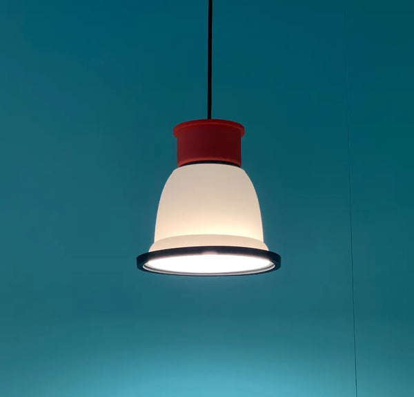 A cute little pendant light by British designer George Sowden. The light is red, white and black. Turquoise background. The light is switched on.