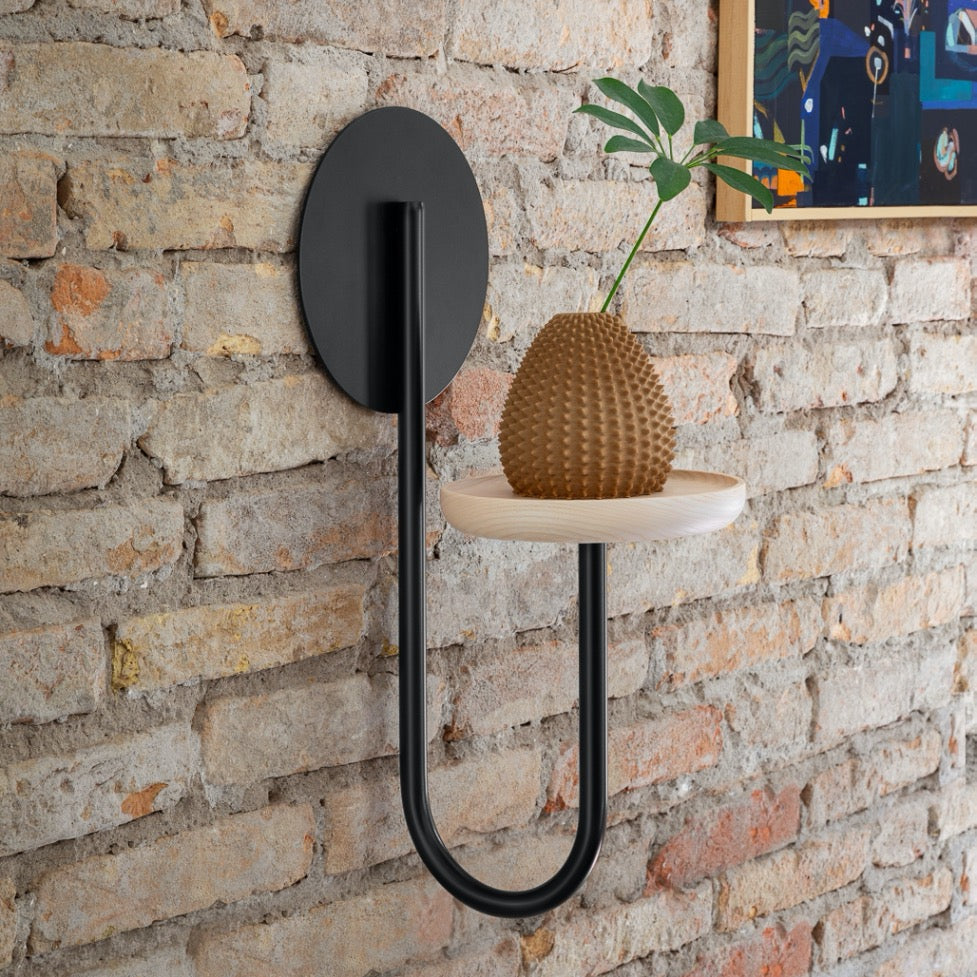 A beautiful wall mounted flowerpot stand. A flower in a pot on the stand. A brick wall.