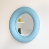 The cutest little wall mirror in mat, baby blue ceramics. The mirror hangs on a white wall.