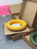 Open cardboard boxes on the floor reveals two super cute and round ceramic mirrors. One is mat yellow and the other mat green.