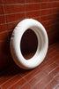 A white, round, ceramic mirror leans up against a tiled wall.