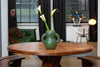 Mat, moss green ceramic vase with bold shapes on a coffee table. Flower in the vase.