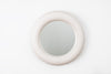 Beautiful, round wall mirror hangs on a white wall. The shape is round and the material is mat, white ceramics.