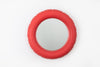 A redish, pink wall mirror. Shape is round. Material is mat ceramics. White background.