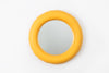 A super cute, round wall mirror on a white wall. The mirror is made from mat, yellow caramic.