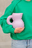 A woman wearing a green jumper and jeans, holds a purple, ceramic water jug.