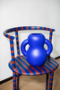 A curvy, navy blue ceramic vase sits on top of a stripy chair. White wall in the background.