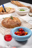 A super cute little ceramic bowl in baby blue on a table next to other food. The bowl is filled with small tomatoes.