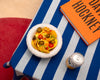 A white, round, ceramic bowl on a table. Tortilla chips and peppers are in the bowl.