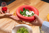 A red, round ceramic bowl filled with yoghurt sauce exchanges hands over a table at a dnner party.