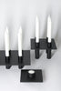 Svartir, skúlptúrískir kertastjakar eftir Nick Ross. Hvítur bakgrunnur. Hvít kerti eru í stjökunum. Sjónarhorn að ofanverðu.