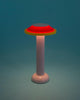 Pretty little table lamp in cute colours. The lamp is red, yellow and pink. Turquoise background. The lamp is switched on.