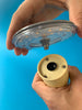 Close-up shot of two hands screwing a small table lamp together. Light blue background.