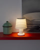 A beautiful little white lamp emits a cozy light. The lamp stands on a red shelf.