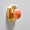 A stunning little wall sconce. Soft shapes. Brushed brass and pink, handmade glass. The sconce is mounted on a white wall.