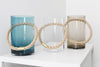 Three glass vases next to each other. From left: turquoise, clear and light brown. Rope handles. White background.