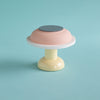A cute and tiny little table lamp in pastel colours. The lamp is bright pink and pale pink with a hint of white. pale turquoise background.
